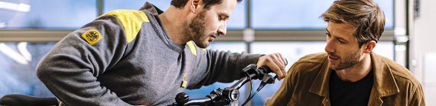 ÖAMTC Techniker betätigt die Bremshebel an einem Fahrradlenker, neben ihm ein Mitglied