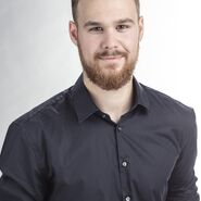 Ein Mann mit kurzen Haaren und Bart, er trägt ein dunkles Hemd.