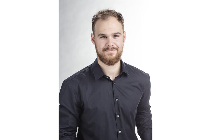 Ein Mann mit kurzen Haaren und Bart, er trägt ein dunkles Hemd.