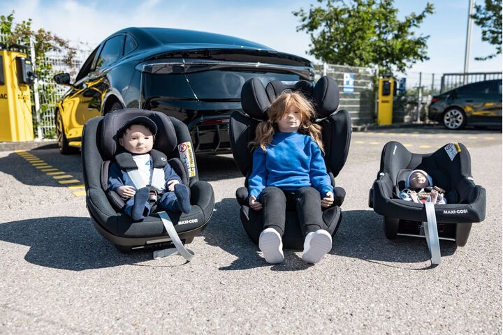 Vor einem Auto stehen drei Kindersitz mit Puppen drinnen.