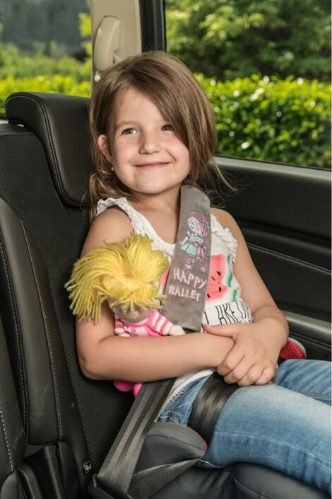 Ein lächelndes Mädchen sitzt im Auto. Auf dem Gurt hat sie den Gurtpolster.