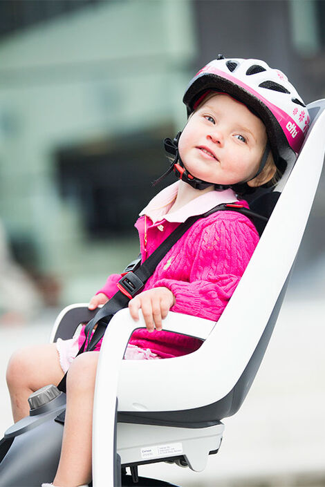 Kleinkind gekleidet in rosa mit einem weiß-rosa Helm sitzt im Fahrradkindersitz.