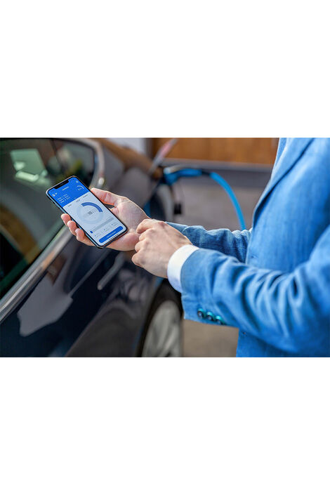 Vor einem E-Auto bedient ein Mann eine Ladeapp am Handy.