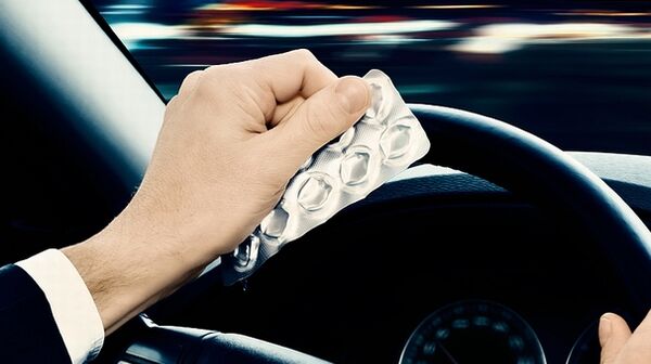 Das Bild zeigt die Hände von einem Autofahrer im Fahrzeug. Er sitzt am Steuer und hält mit einer Hand das Lenkrad, während er in der linken Hand ein Tablettenblister hält.