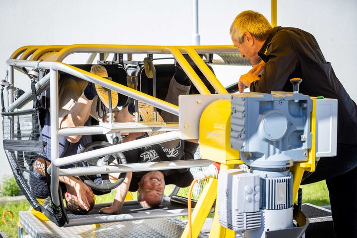 Zwei Personen, die im ÖAMTC Fahrtechnik Überschlagssimulator sitzen und sich überschlagen, begleitet von einem Mitarbeiter der ÖAMTC Fahrtechnik.