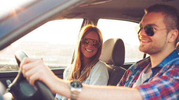 Zwei Jugendliche (ein Mann und eine Frau) sitzen im Fahrersitz im Auto.