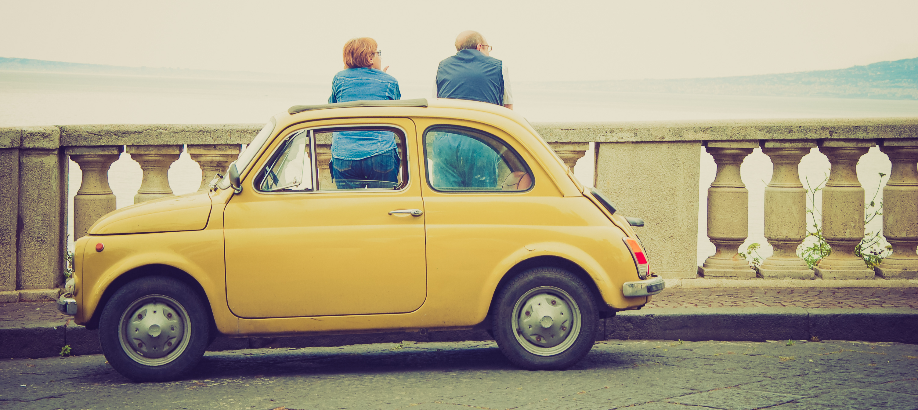 Ein Fiat 500 Oldtimer steht auf einer Brücke, während zwei Personen die Aussicht genießen.