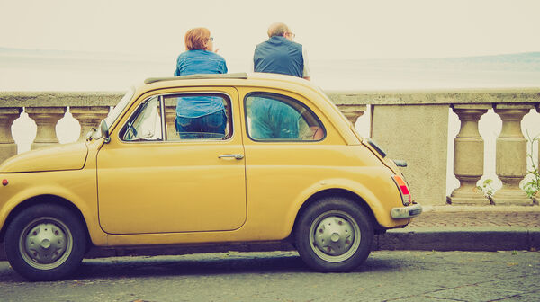 Ein Fiat 500 Oldtimer steht auf einer Brücke, während zwei Personen die Aussicht genießen.