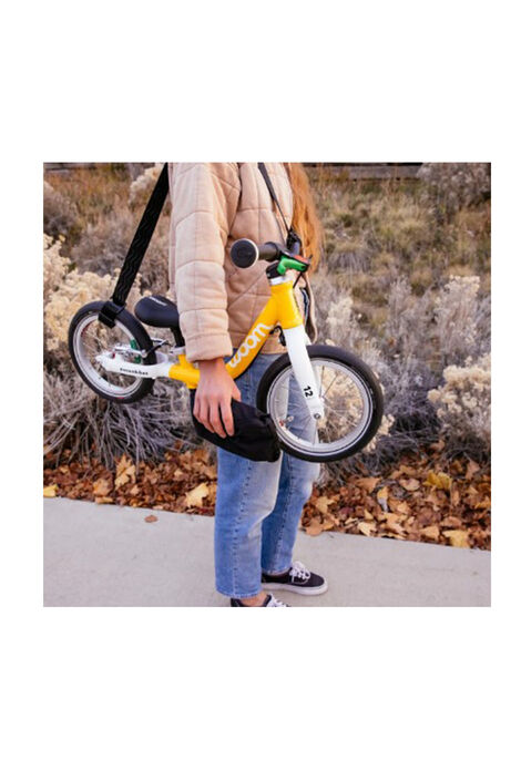 Frau trägt Laufrad von Woom mit dem Tragegurt über ihrer Schulter und hält in ihrer Hand die zusammengefaltete Tragetasche