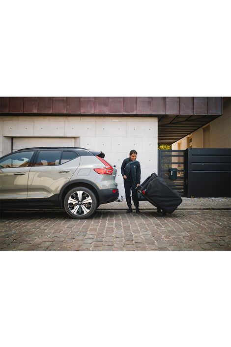 Eine Frau zieht das Thule Outset in der Reiseverpackung mithilfe der Rollen zu ihrem Auto.