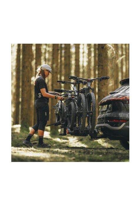 Eine Frau im Wald fixiert 3 Räder auf dem Fahrradträger ihres Autos.