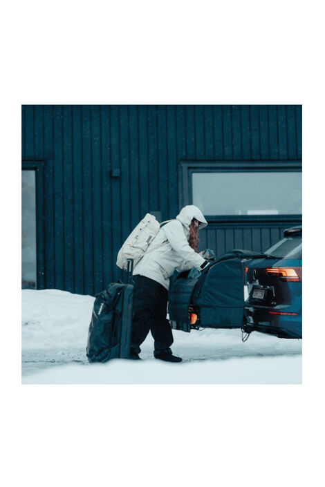 Eine Person in einer Winterjacke steht vor dem Ladungsträger und verstaut Koffer darin.