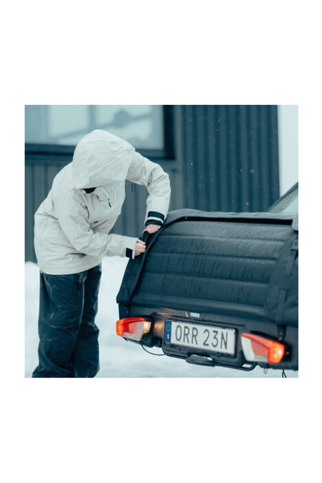 Eine Person in Winterjacke schließt den Ladungsträger. Die Rücklichter leuchten und das Kennzeichen ist zwischen den Lichtern montiert.