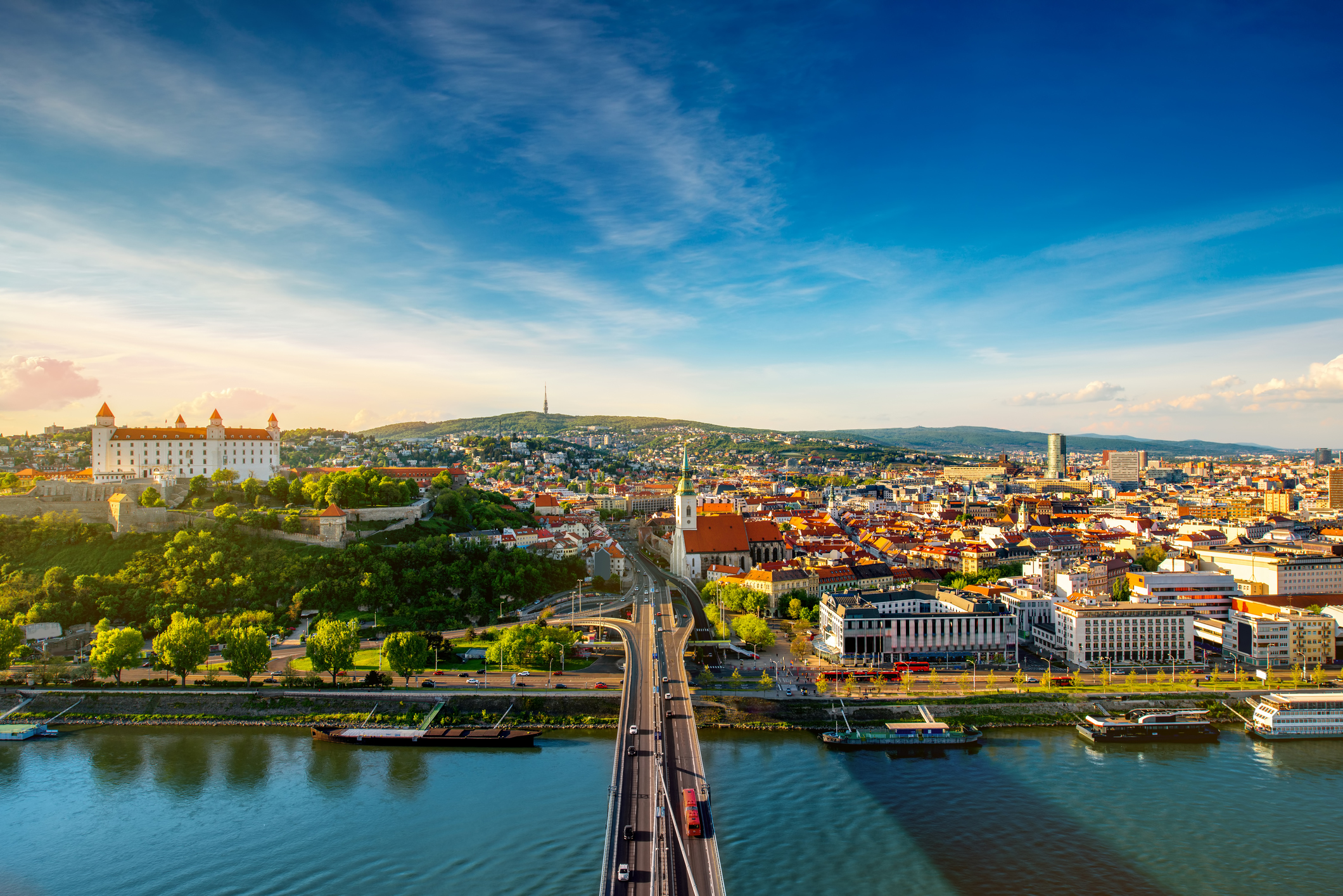 Panoramablick auf Bratislava, die Hauptstadt der Slowakei, bei sonnigem Wetter. Im Vordergrund verläuft die Brücke über die Donau, die die beiden Stadtteile verbindet. Links auf dem Hügel sieht man die Bratislavaer Burg.