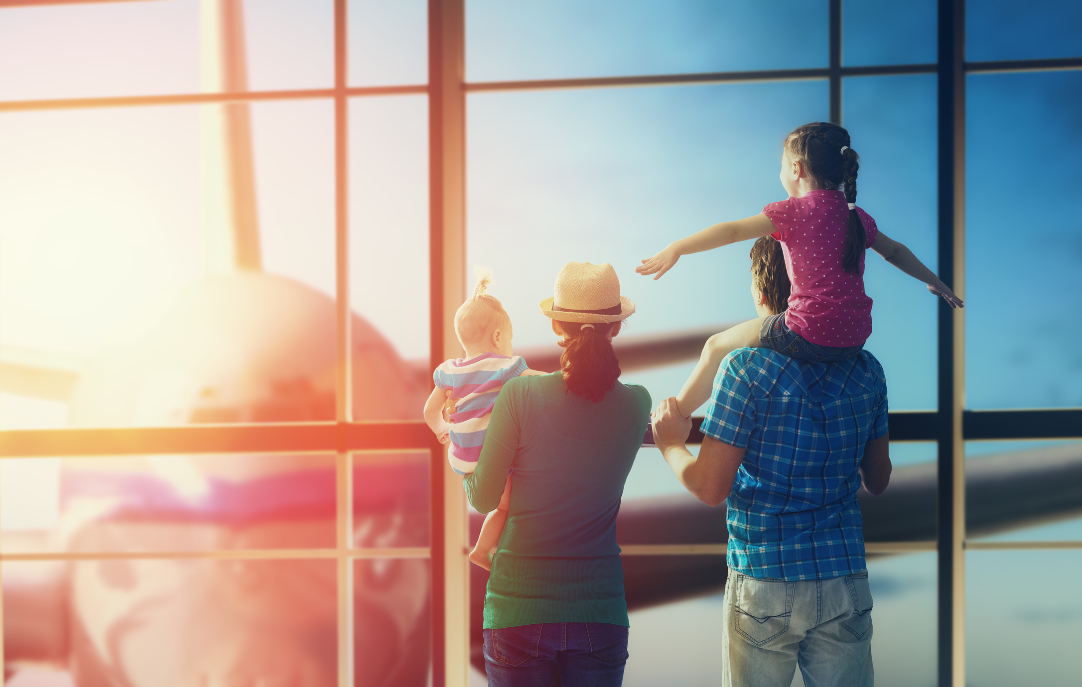 Eine Familie mit zwei Kindern schaut durch ein Flughafenfenster auf ein Flugzeug.