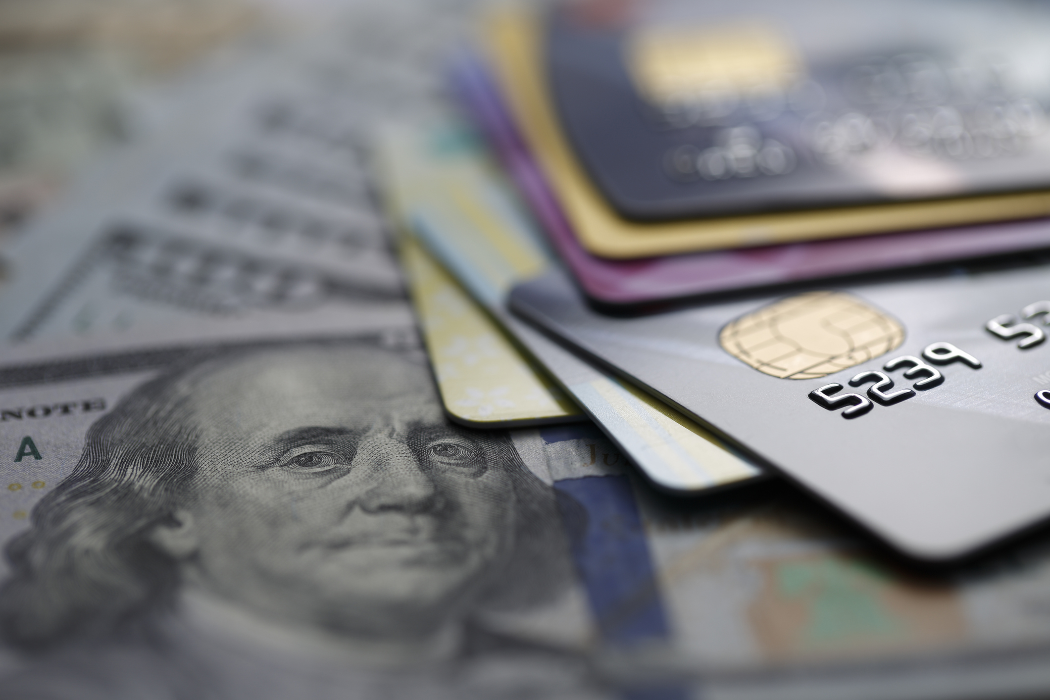 Mehrere Kreditkarten, die auf einem Haufen Geldscheine liegen, darunter ein 100-Dollar-Schein mit Benjamin Franklins Porträt.