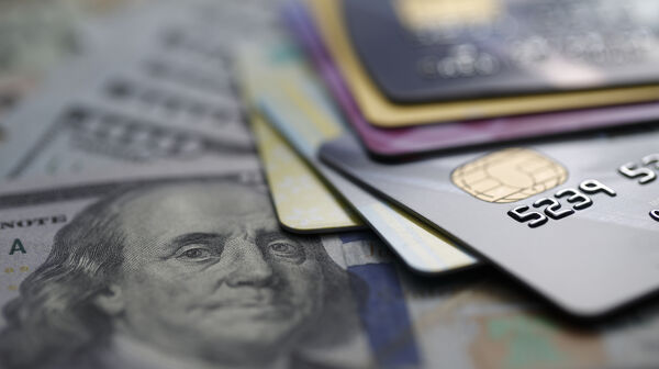 Mehrere Kreditkarten, die auf einem Haufen Geldscheine liegen, darunter ein 100-Dollar-Schein mit Benjamin Franklins Porträt.