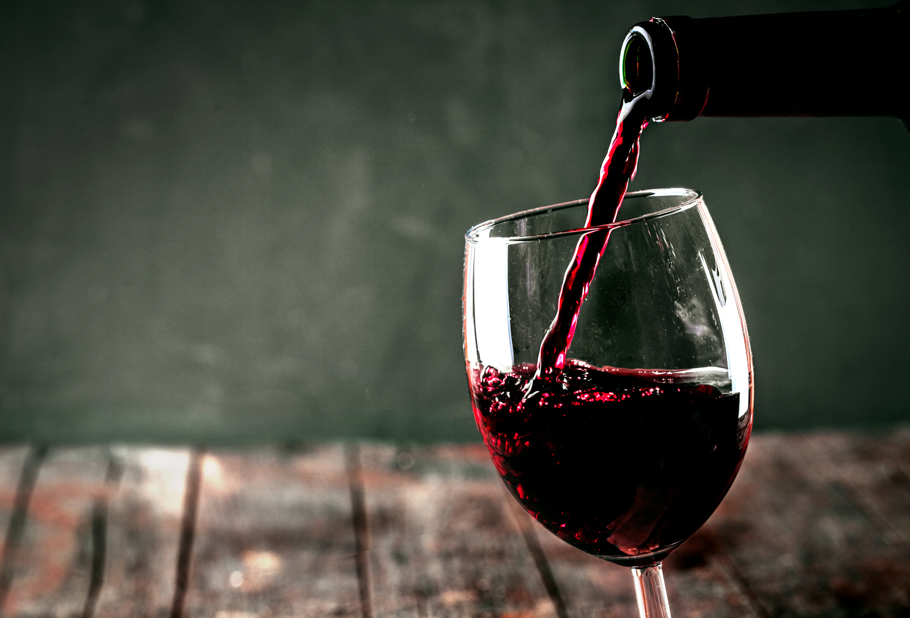 Es wird gerade aus einer Glasflasche Rotwein in ein Weinglas geleert.