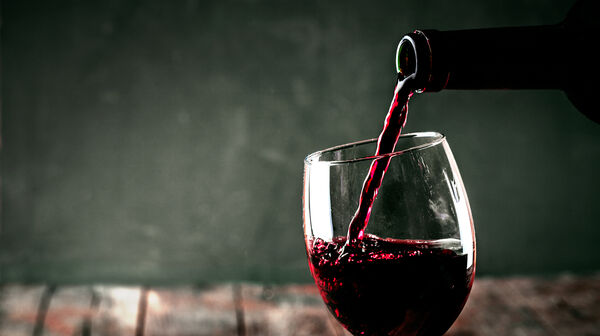 Es wird gerade aus einer Glasflasche Rotwein in ein Weinglas geleert.