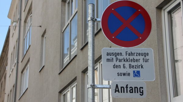 Das Bild zeigt ein Parkverbotsschild mit zwei Zusatztafeln in Wien. Auf dem oberen Zusatzschild steht: "ausgen. Fahrzeuge mit Parkkleber für den 6. Bezirk sowie" und zeigt ein Symbol für einen Behindertenparkplatz. Das untere Zusatzschild zeigt das Wort "Anfang“.