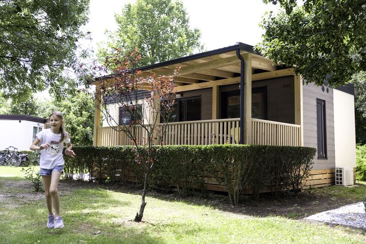 Das Bild zeigt ein Mobilheim auf einem Campingplatz. Links im Bild läuft ein Kind.