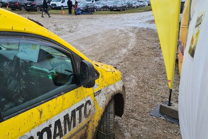 Ein schmutziges ÖAMTC-Fahrzeug steht auf einem matschigen Parkplatz, im Hintergrund sind andere Autos zu sehen.