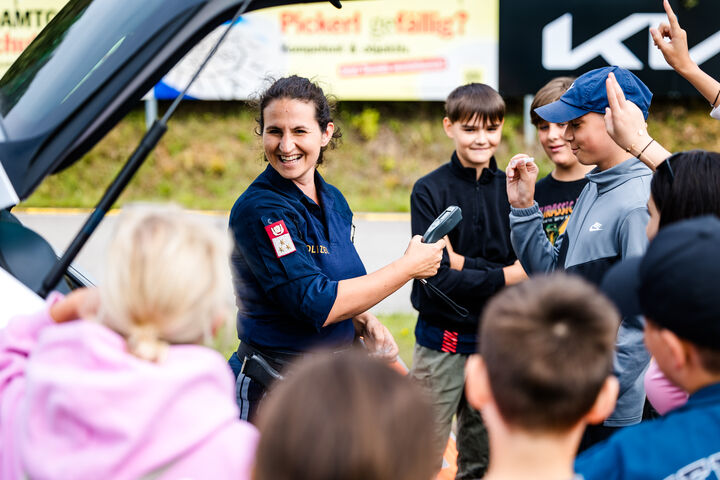 Polizistin und Kinder stehen um ein Auto mit geöffneter Motorhaube