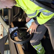 Ein Pannenfahrer sitzt in einem Elektroauto und führt mittels Tablet eine Fahrzeugdiagnose bzw. Pannendiagnose durch.