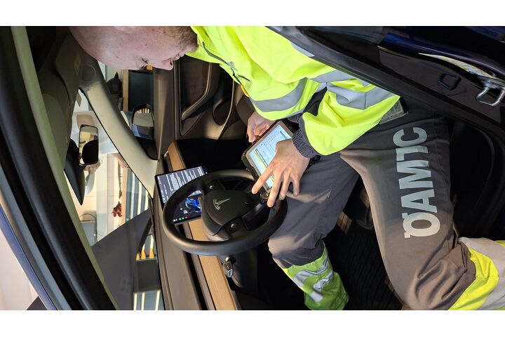 Ein Pannenfahrer sitzt in einem Elektroauto und führt mittels Tablet eine Fahrzeugdiagnose bzw. Pannendiagnose durch.