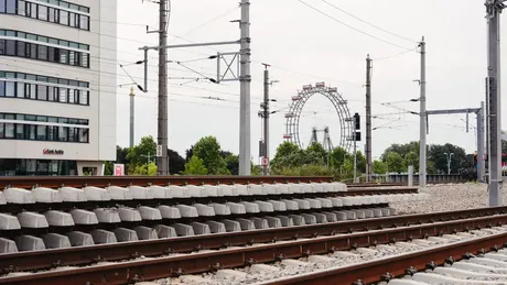 Zugschienen und Strecke, im Hintergrund ein Hochhaus und Stromleitungen.