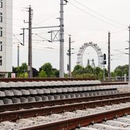 Zugschienen und Strecke, im Hintergrund ein Hochhaus und Stromleitungen.