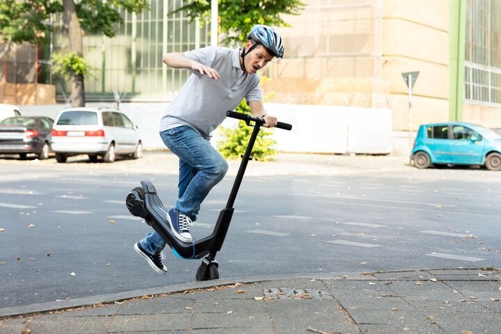 Männlicher E-Scooter-Fahrer mit Helm stürzt über Bordsteinkante