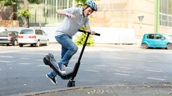 Männlicher E-Scooter-Fahrer mit Helm stürzt über Bordsteinkante