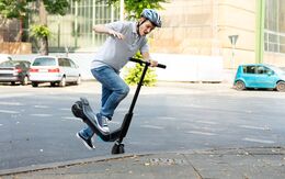 Männlicher E-Scooter-Fahrer mit Helm stürzt über Bordsteinkante