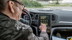 Innenansicht eines Autos. Ein Mann bedient die Klimaanlage am Display.