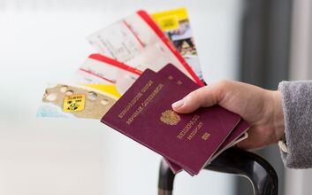 Eine Hand hält zwei österreichische Reisepässe, Tickets und Folder, darunter sieht man den Griff von einem Koffer.