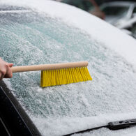 Die Windschutzscheibe eines Autos wird mit einem Besen von Schnee befreit