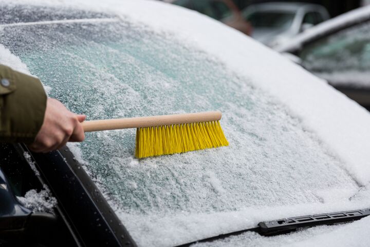 Die Windschutzscheibe eines Autos wird mit einem Besen von Schnee befreit