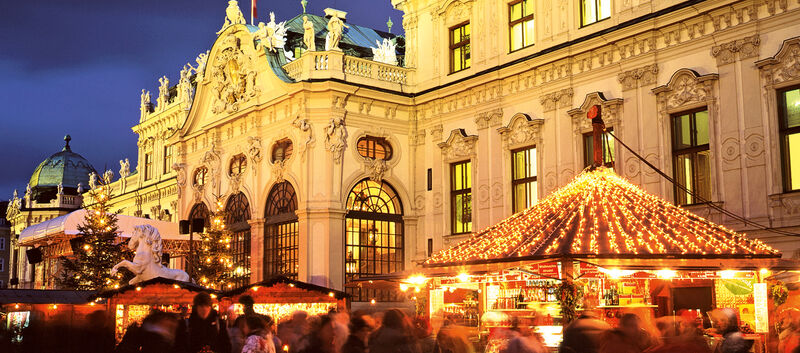 In der Abenddämmerung ein hell beleuchteter Weihnachtsmarkt vor einem schönen, großen, alten Schloss.