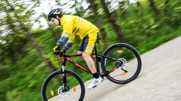 Ein Mann in Fahrraddress und Helm fährt mit dem Fahrrad auf einer Straße.