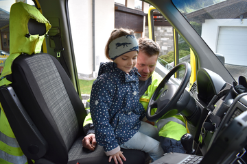 Ein Kindergartenkind sitzt auf dem Fahrersitz des Pannenfahrzeugs und Pannenfahrer Thomas erklärt, was sich alles im Innenraum befindet. 
