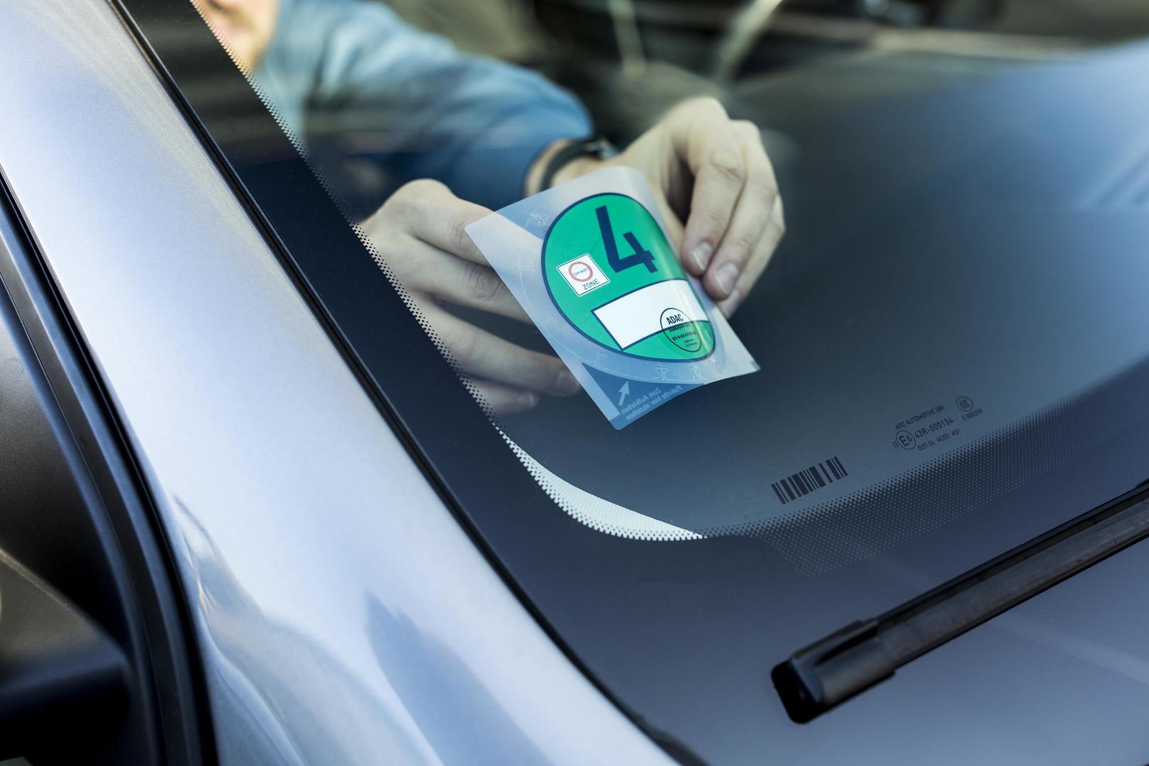 Ein Mensch klebt gerade eine Umweltplakette auf die Innenseite der Autofrontscheibe .
