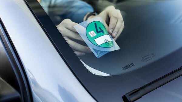 Ein Mensch klebt gerade eine Umweltplakette auf die Innenseite der Autofrontscheibe .