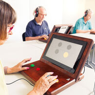 Senioren sitzen an Tischen vor Laptop-ähnlichen Geräten und machen Reaktionstests