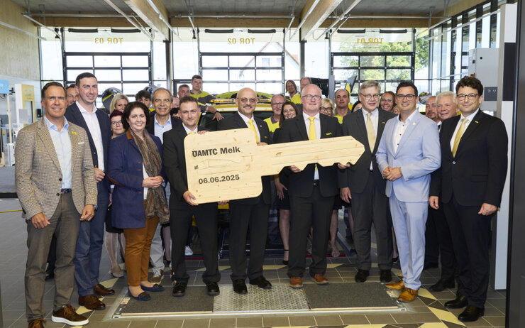 Eröffnung Stützpunk Melk Feierliches Gruppenfoto in der Prüfhalle. Einige stehen zusammen und halten einen großen Holzschlüssel.