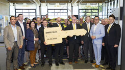 Feierliches Gruppenfoto in der Prüfhalle. Einige stehen zusammen und halten einen großen Holzschlüssel.