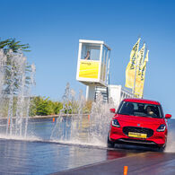 Ein rotes Auto weicht einer Wasserfontäne auf einer Piste in einem Fahrtechnik Zentrum aus