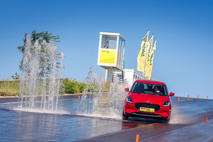 Ein rotes Auto weicht einer Wasserfontäne auf einer Piste in einem Fahrtechnik Zentrum aus