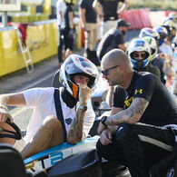 Zwei Kart-Fahrer eines Teams beim Gespräch in der Boxengasse, einer sitzt im Kart, der andere hockt daneben.