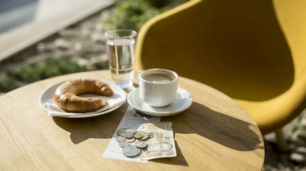 Kaffee und Croissant auf einem Café-Tisch mit Trinkgeld in Form von Münzen und einem Geldschein